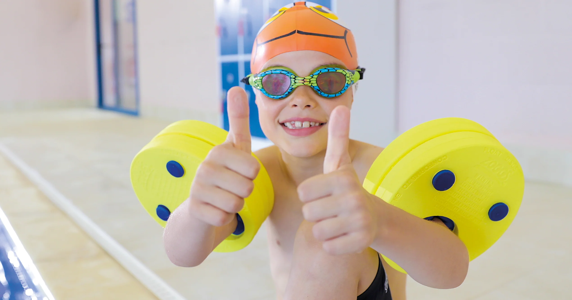 Child with swimming armbands giving thumbs up by the pool